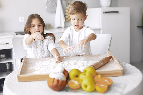 Cute little children sitting in a kitchen with dough - Foto, afbeelding