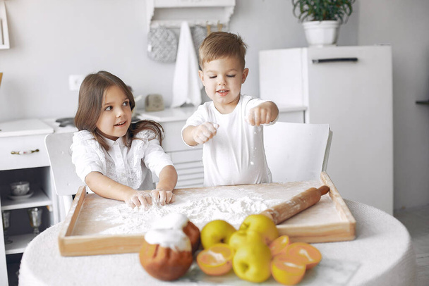 Cute little children sitting in a kitchen with dough - Фото, зображення