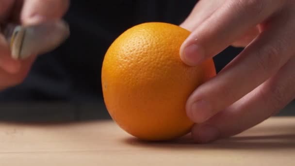 Vista cercana de una mano cortando una naranja por la mitad para hacer jugo fresco en la tabla de cortar
. - Metraje, vídeo