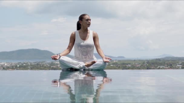 Spokojna kobieta praktykująca jogę w lotosowym basenie postawy przeciwko niebu - Materiał filmowy, wideo