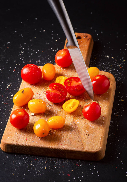 Different tomatoes cultivars on a wooden board on the black background. Multicolor tomatoes - Foto, Bild