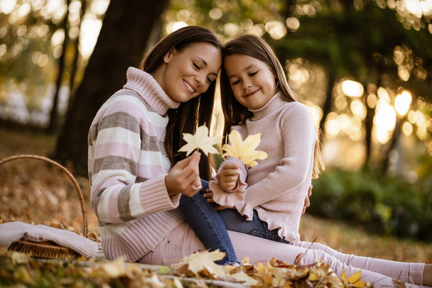Mother and daughter enjoying autumn in park. - 写真・画像