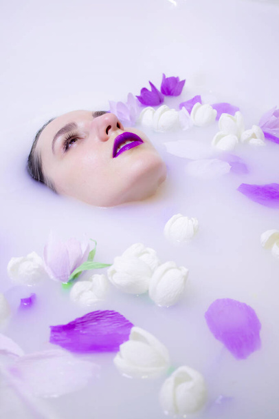  Modelmädchen mit violettem Make-up im Milchbad mit violetten Blüten - Foto, Bild
