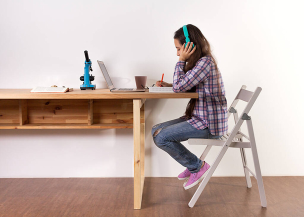 Distance learning.Home schooling, young teen girl studying at a laptop, listening to music with headphones, watching a webinar online, doing science and biology. Elearning concept. - Foto, Bild