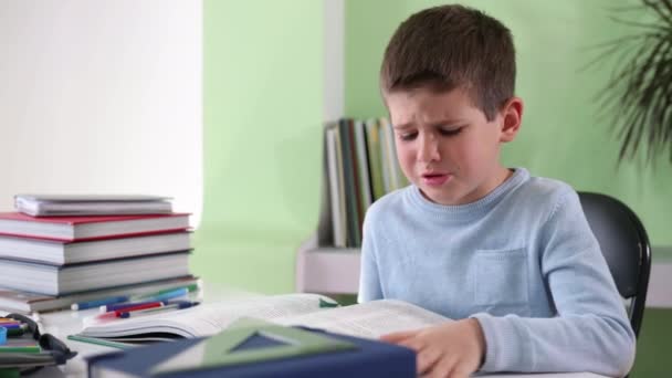 domácí vzdělání, rozrušený unavený dítě dělá domácí úkoly, čte knihu a rekvizity jeho čelo rukou, zatímco sedí u stolu se školními potřebami, tvrdé učení - Záběry, video