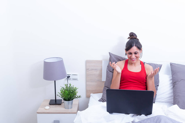 Feliz sorrindo jovem mulher, relaxando em sua cama com laptop computer.Opening braços surpreendidos
. - Foto, Imagem