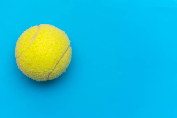 コピースペースでスポーツやアクティビティを象徴するソリッドアクアブルーのフラットレイアウトの背景に明るい黄色のテニスボール. - 写真・画像