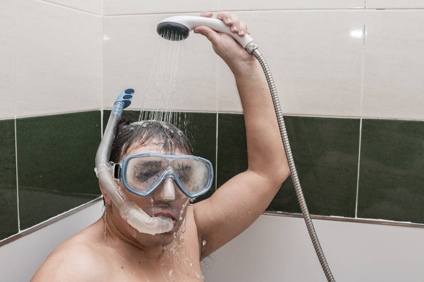 Hombre maduro en gafas con snorkel vertiendo agua limpia en la cabeza mientras descansa en el baño en lugar de la playa durante la cuarentena
 - Foto, imagen