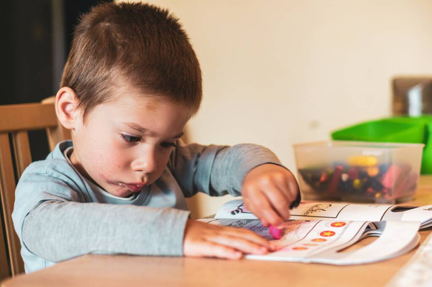 POZNAN, POLAND - Apr 13, 2020: Small two years old boy sitting by a table and coloring a Thomas and Friends book. - Photo, Image