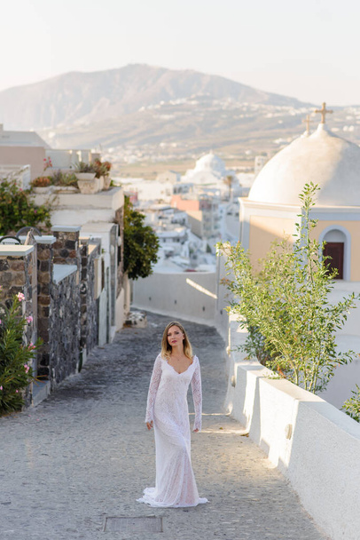 Hermosa novia en un vestido blanco posando sobre el telón de fondo de la ciudad de Thira, Santorini
. - Foto, Imagen