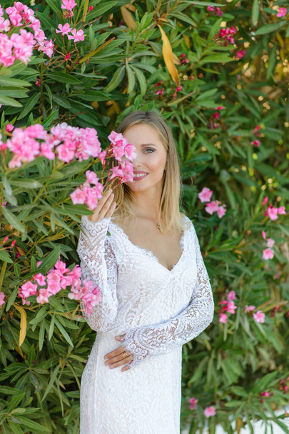 Πορτρέτο μιας όμορφης νύφης με λευκό φόρεμα σε θάμνο με λουλούδια. - Φωτογραφία, εικόνα