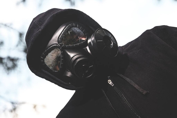 A low angle shot of a person wearing a gas mask and black jacket in the ranch during a quarantine - Photo, image