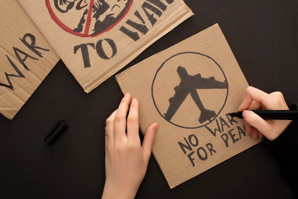 oříznutý pohled na ženu kreslení plakátu bez války za mír písmo a letadlo na černém pozadí - Fotografie, Obrázek