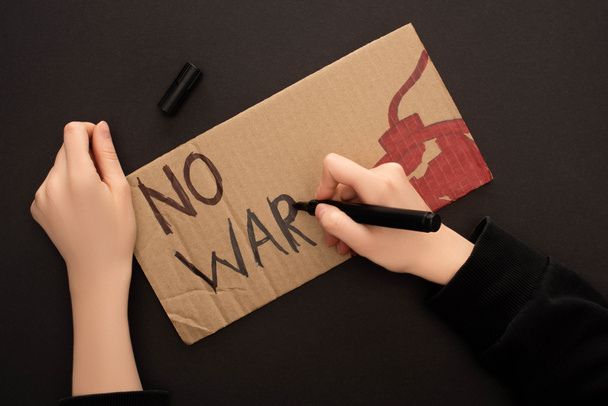 cropped view of woman drawing placard with no war lettering and bomb on black background - Foto, Imagem