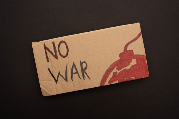 top view of cardboard placard with no war lettering and bomb on black background - Foto, immagini