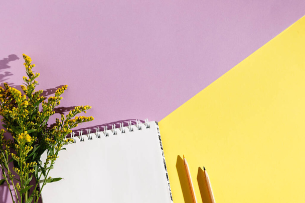 Пустая белая винтажная тетрадь, листья, желтые цветы, дневник на фиолетовом желтом фоне. Минималистическая концепция рабочего места. Вид сверху с пространством для копирования. Летняя квартира
 - Фото, изображение