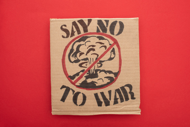 top view of cardboard placard with say no war to war lettering and explosion in stop sign on red background - Photo, Image