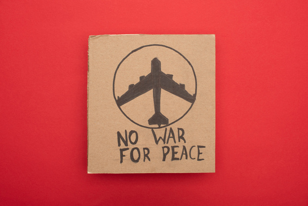 vista superior del cartel de cartón sin letras de guerra para la paz y el avión sobre fondo rojo
 - Foto, Imagen