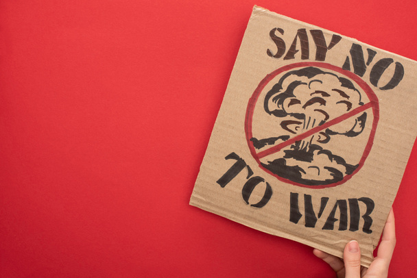 partial view of woman holding cardboard placard with say no war to war lettering and explosion in stop sign on red background - Фото, изображение