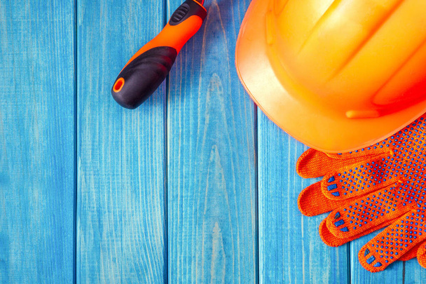 Orange hard hat and tool on wooden vintage blue boards. Protective equipment for the builder - 写真・画像