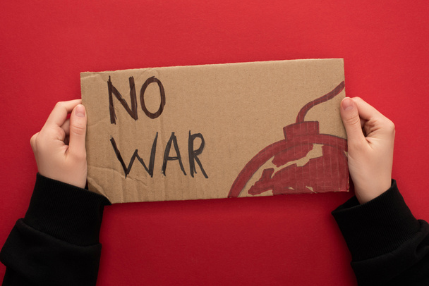 abgeschnittene Ansicht einer Frau mit Pappplakat ohne Kriegsbeschriftung und Bombe auf rotem Hintergrund - Foto, Bild