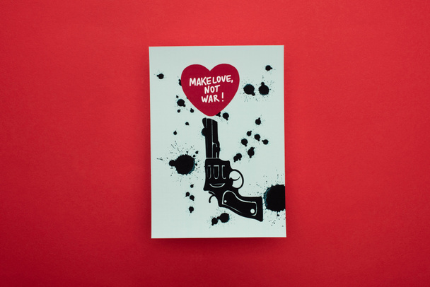 top view of white paper with drawn black revolver and heart with make love not war lettering on red background - Foto, afbeelding