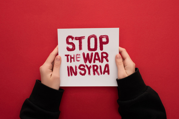 Teilansicht einer Frau mit weißem Plakat mit dem Schriftzug "Stoppt den Krieg in Syrien" auf rotem Hintergrund - Foto, Bild