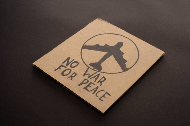 cardboard placard with no war for peace lettering and airplane on black background - Fotografie, Obrázek