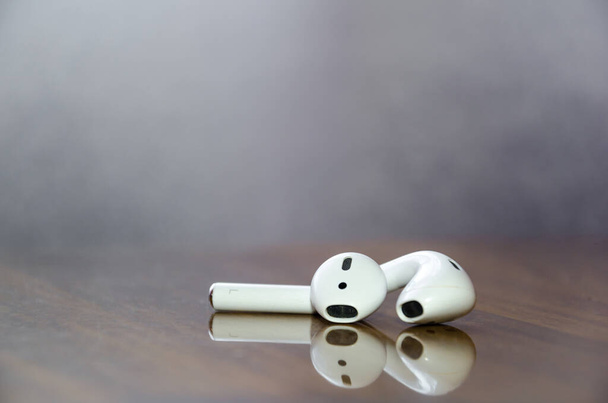 Roztroušená bílá bezdrátová sluchátka na stole s odrazem. - Fotografie, Obrázek