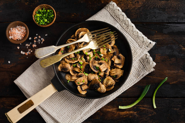 Fried Champignon mushrooms in a cast-iron old pan on an old dark wooden rustic background for frying. Top view. - Foto, Imagem