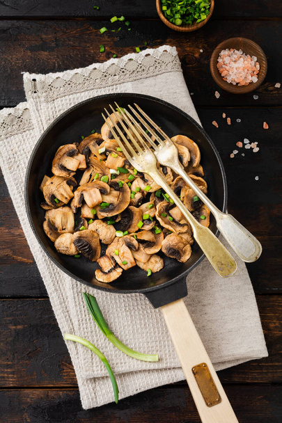 Fried Champignon mushrooms in a cast-iron old pan on an old dark wooden rustic background for frying. Top view. - Foto, immagini