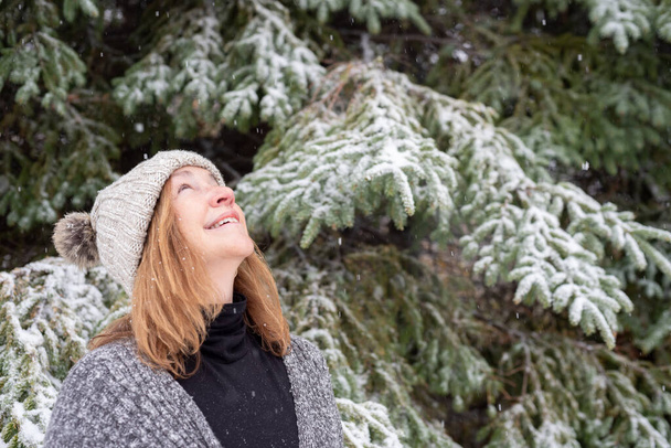 donna felice guardando i fiocchi di neve che cadono nella pineta in inverno
 - Foto, immagini