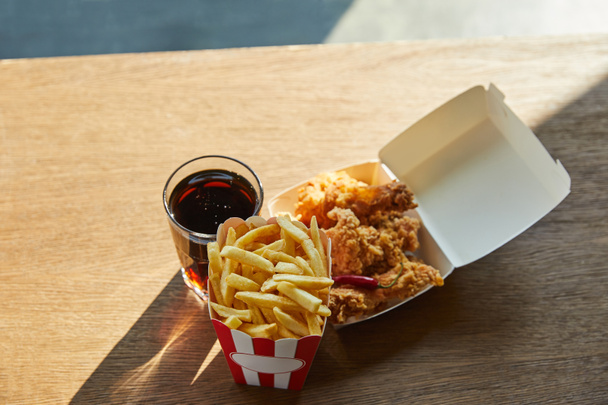 deep fried chicken, french fries and soda in glass on wooden table in sunlight - Photo, Image