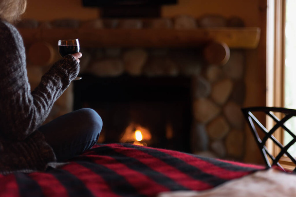 κάθεται δίπλα στη φωτιά με ένα ποτήρι κρασί - Φωτογραφία, εικόνα