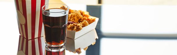 deep fried chicken, striped bucket and soda in glass on glass table in sunlight near window, panoramic orientation - Photo, Image