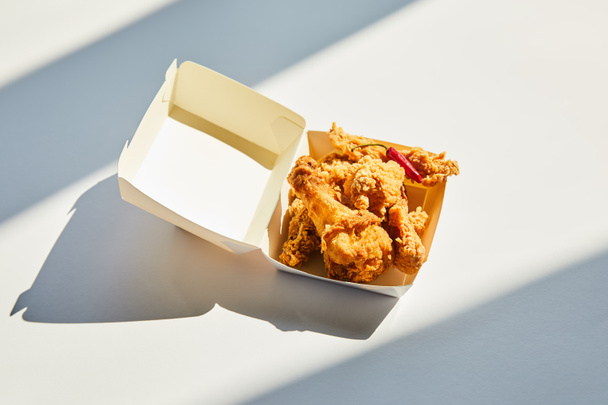 tasty and spicy deep fried chicken with chili pepper on white table in sunlight - Foto, Imagem