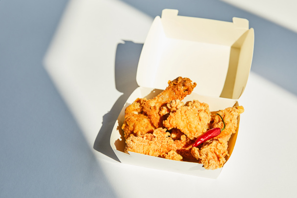 вкусная и пряная курица во фритюре с перцем чили на белом столе при солнечном свете
 - Фото, изображение