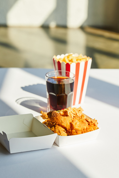 selective focus of tasty deep fried chicken, french fries and soda in glass on white table in sunlight - Photo, Image