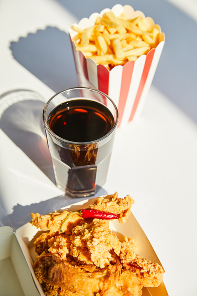 selective focus of tasty deep fried chicken, french fries and soda in glass on white table in sunlight - 写真・画像