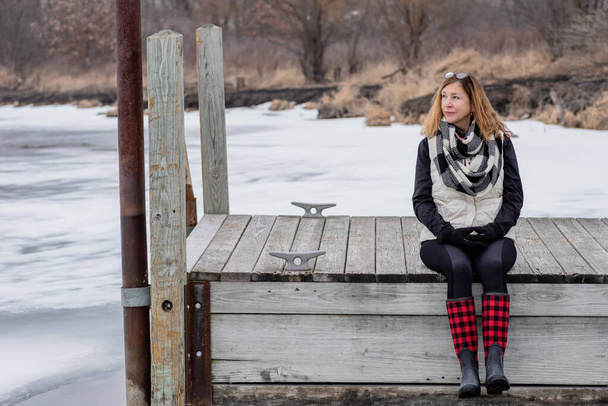 person sitting on wooden dock in winter looking out at frozen lake in Illinois - Photo, Image