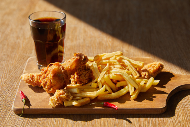 poulet frit épicé, frites à bord avec soda en verre sur table en bois au soleil
 - Photo, image