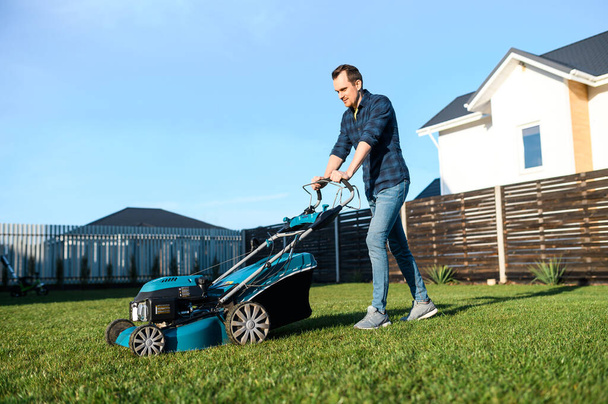 Young man in a plaid shirt and jeans mows lawn - Foto, Imagem