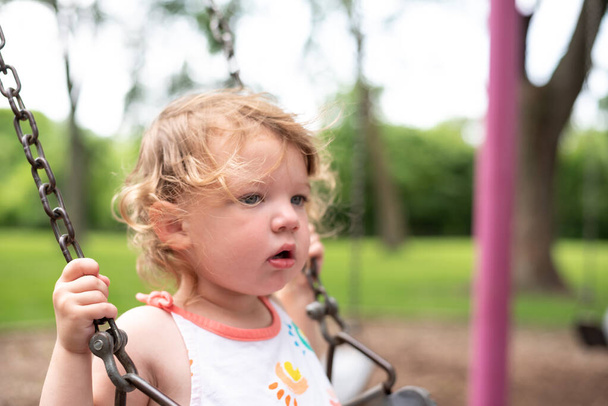 κοντινό πορτρέτο του μικρού κοριτσιού σε κούνια στην παιδική χαρά - Φωτογραφία, εικόνα