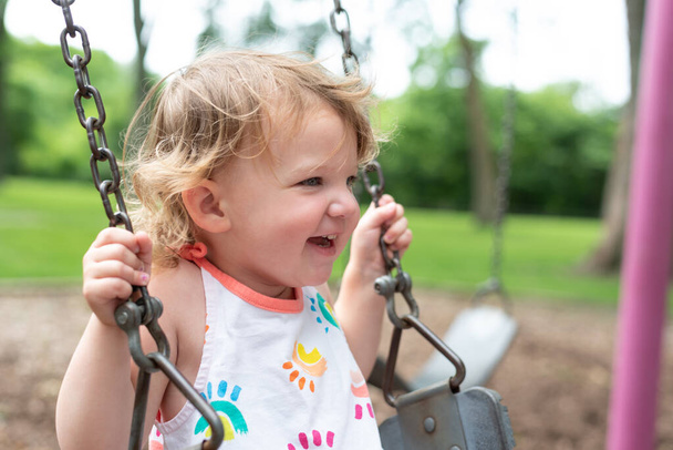 fröhliches Kind spielt an einem Sommertag auf Schaukel auf Spielplatz im Park - Foto, Bild