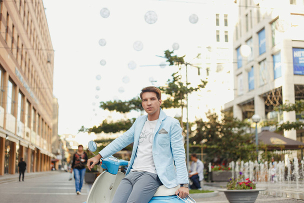 Молодой человек в синем платье позирует на скутере в городе
 - Фото, изображение