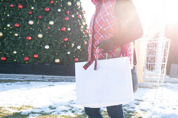 donna che tiene la borsa della spesa camminando davanti all'albero di Natale al centro commerciale all'aperto nella giornata di sole
 - Foto, immagini