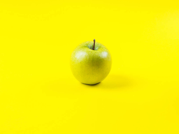 Shiny green apple on bold yellow background - Foto, afbeelding