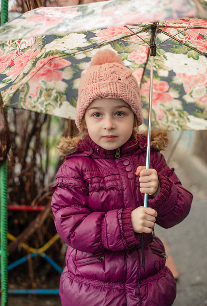 Dışarıda şemsiyenin altında küçük bir kız, yağmurlu bir gün. Küçük kız yağmurun altında şemsiyeyle yürür. Yağmurlu bir günde pembe şapkalı ve mor ceketli bir çocuk. - Fotoğraf, Görsel