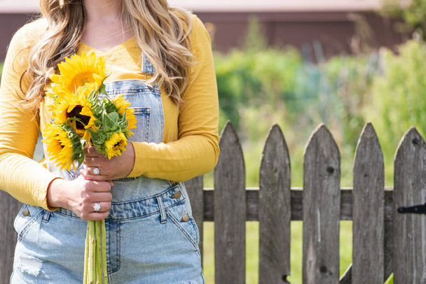 junge Frau in Overalls mit Sonnenblumen im Garten - Foto, Bild