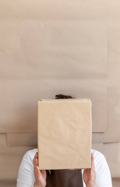 Handen van de verpakking met een papieren zak en doos. Werknemer gekleed in bruin schort Verpakking Order for Customer. - Foto, afbeelding